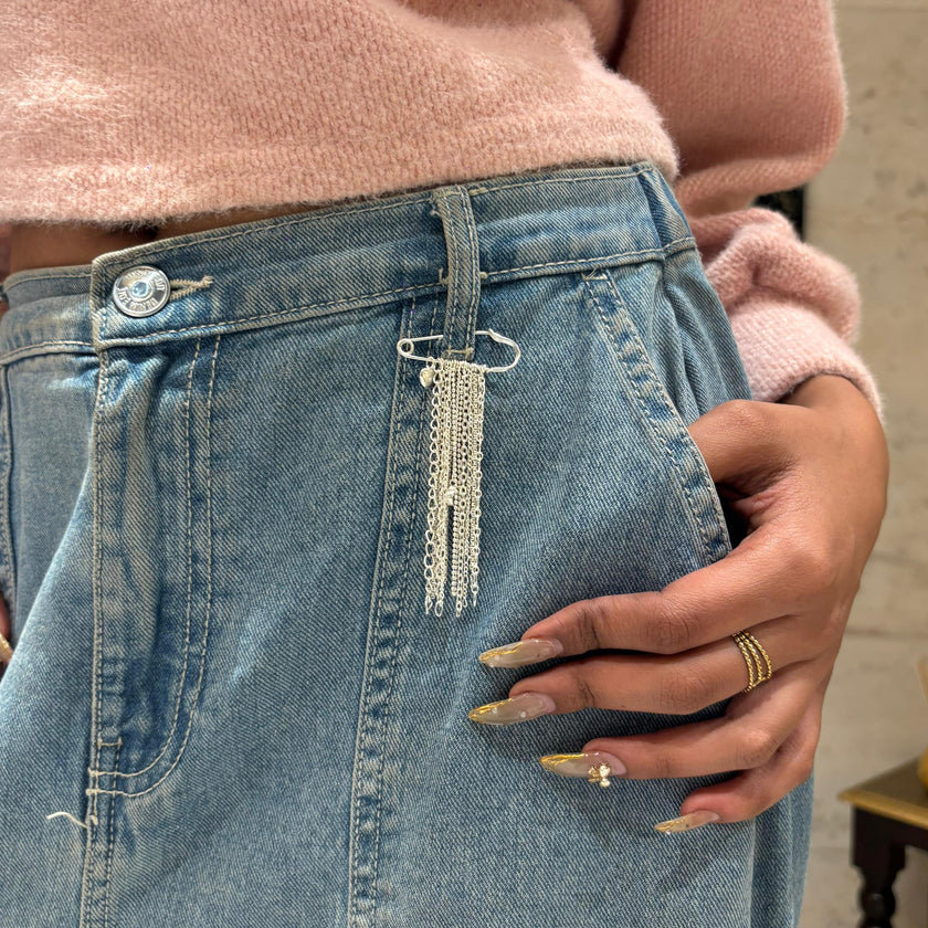 Person wearing a pink sweater and light blue jeans with a chain detail, standing indoors.