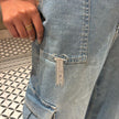 Close-up of a person wearing light blue jeans with a decorative chain on the pocket, standing on a patterned floor.