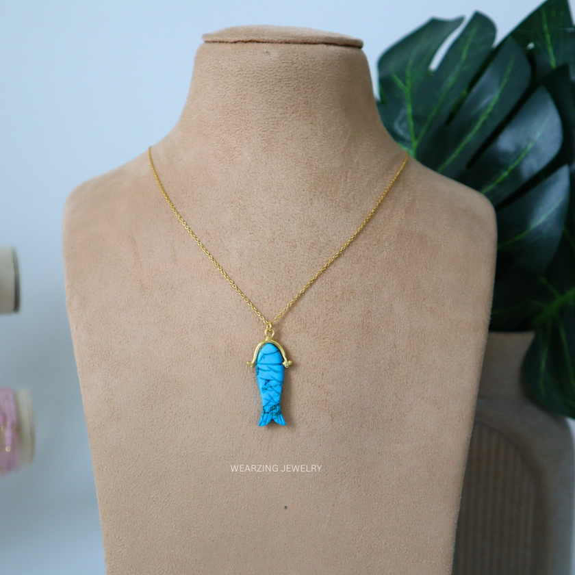 Blue fish-shaped pendant on a gold chain displayed on a mannequin bust.