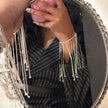 Person wearing a black pinstripe outfit with silver fringe details, reflected in an ornate mirror.