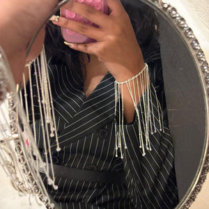 Person wearing a black pinstripe outfit with silver fringe details, reflected in an ornate mirror.