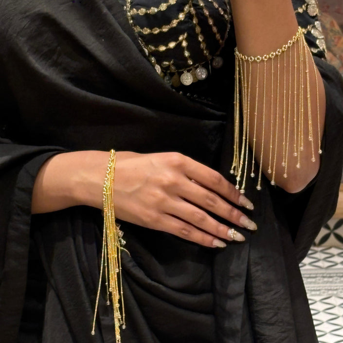 Person wearing a black outfit with gold embroidery and gold jewelry, including bracelets and bangles.