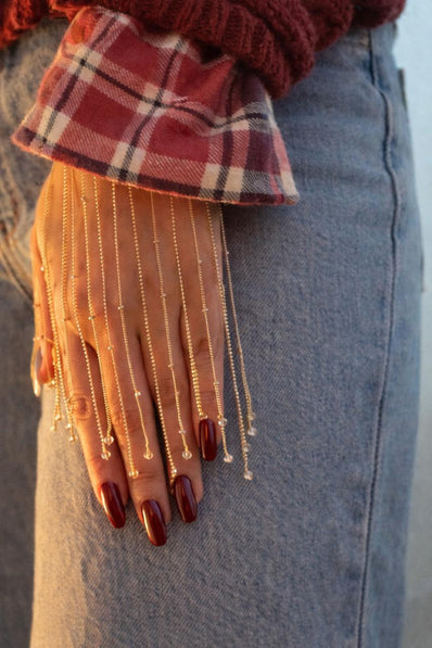 Close-up of a hand wearing gold chain gloves with plaid fabric on a blurred background