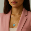 Woman wearing a pink blazer with a gold necklace featuring a blue pendant.